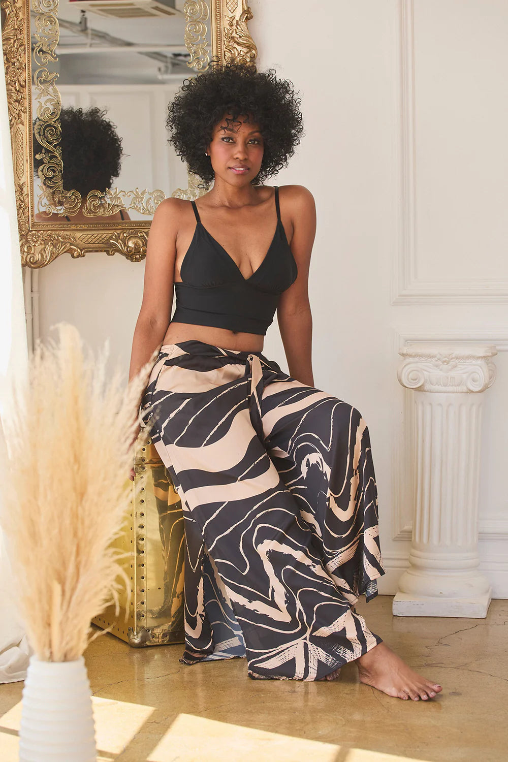 Woman in black top and patterned pants sitting in a room with decorative elements.